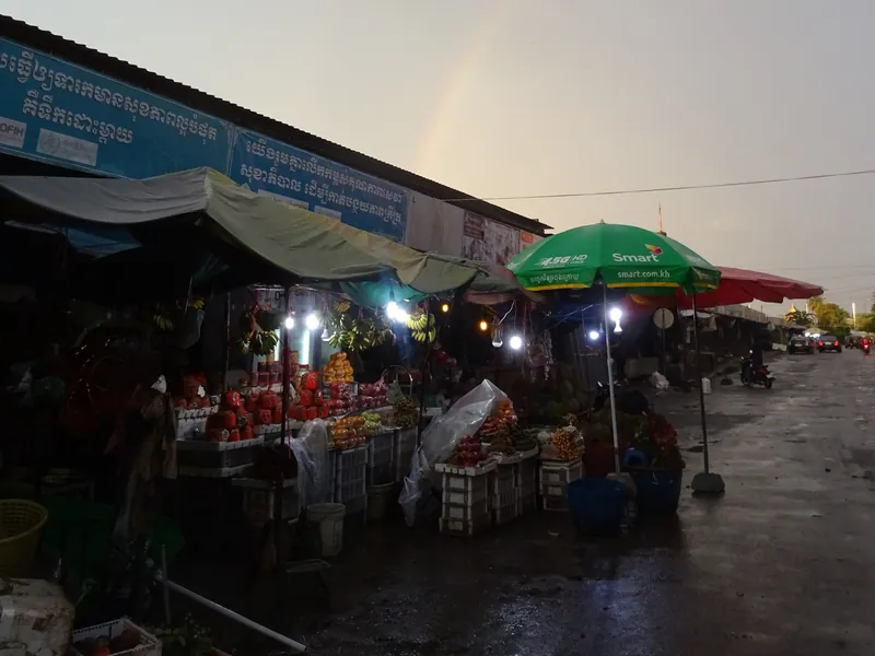 Fruit and vegetable stalls at Phsar Nat central market in Battambang after a rain shower, with a rainbow