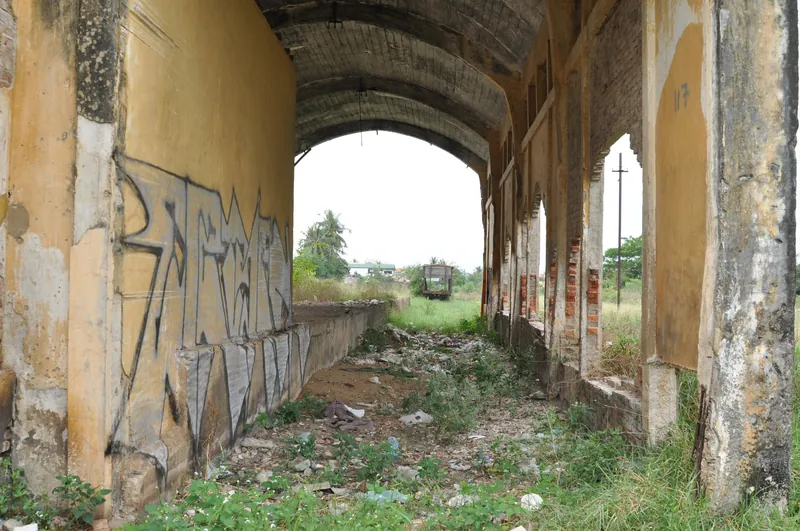 Battambang station's goods shed without tracks, with rubble, graffiti and overgrowth. The line lay idle for decades; passenger service to Phnom Penh only resumed in 2018.