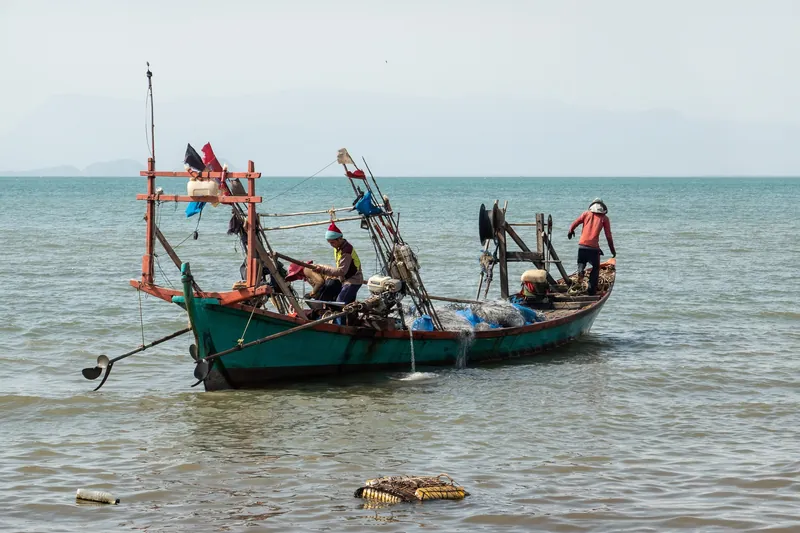 Fischerboot vor der Küste von Kep, im Vordergrund treibt eine Plastikflasche im Wasser