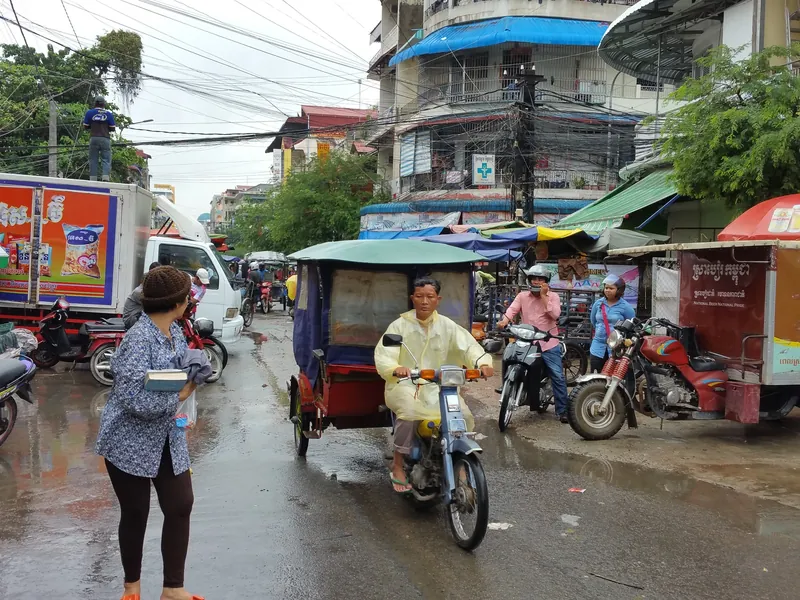 Nasse, von Pfützen bedeckte Straße mit Tuk-Tuk und Motorrädern in Phnom Penh (Straßen stehen nach starken Regenfällen unter Wasser, vor allem in der Regenzeit Mai bis Oktober)