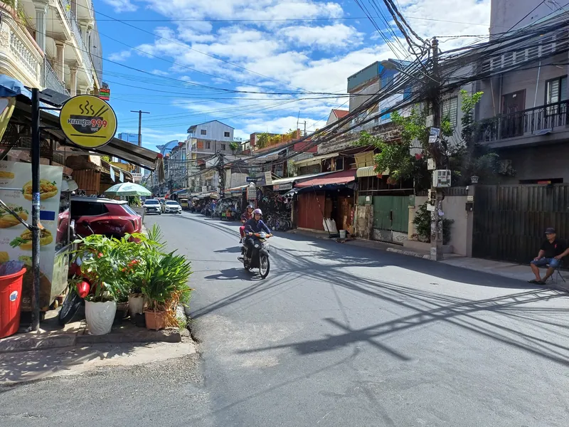 Side street in Phnom Penh with a motorbike, a street kitchen and bundled overhead cables