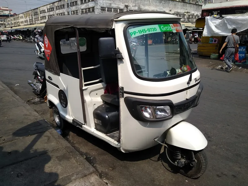 Tuk-Tuk (Auto-Rikscha) mit Aufklebern der Fahrdienst-Apps Grab und PassApp am Straßenrand in Phnom Penh