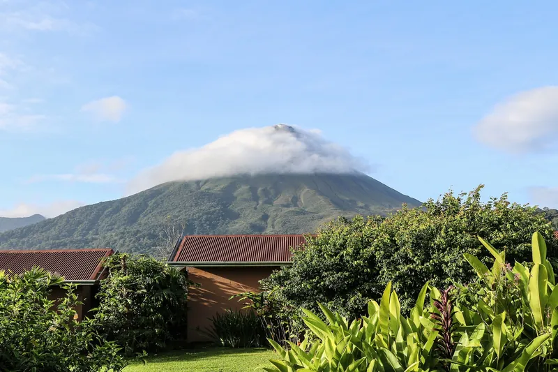 Wohnhäuser mit Wellblechdächern und Gartenbepflanzung vor dem Vulkan Arenal bei La Fortuna