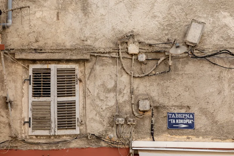 Rendered house front with shutters, overhead cables and a taverna sign in Corfu Town's old town