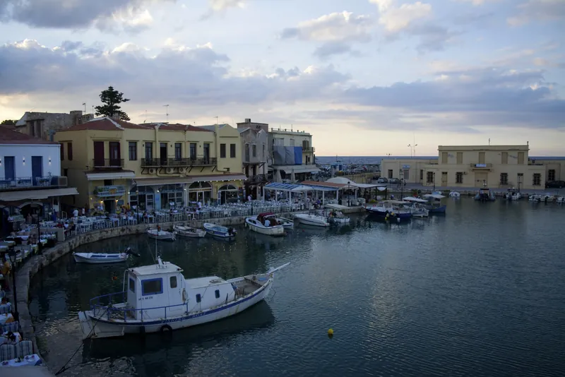 Venezianischer Hafen von Rethymno auf Kreta mit Fischerbooten und Tavernenterrassen in der Abenddämmerung