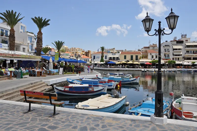 Old harbour at Lake Voulismeni in Agios Nikolaos, Crete, with fishing boats and tavernas on the promenade