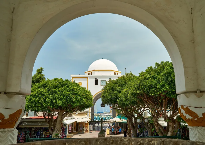 Torbogen und Läden der Markthalle Nea Agora am Mandraki-Hafen in Rhodos-Stadt