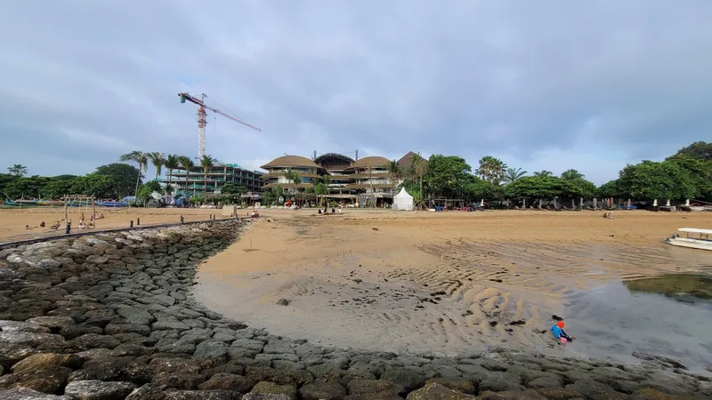 Baukran über einem Hotelneubau direkt am Strand von Sanur hinter einer Steinschüttung zum Küstenschutz (Beispiel für die Bautätigkeit an der Küste)