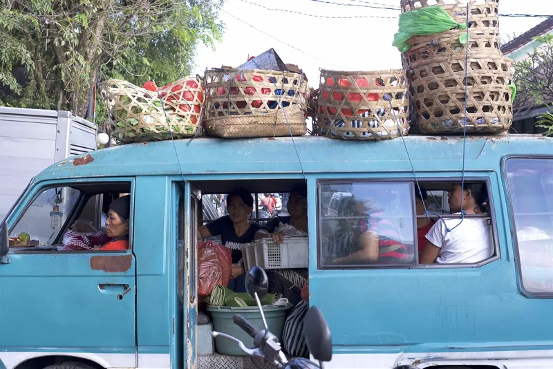 Voll besetzter Bemo (öffentlicher Kleinbus) mit Körben auf dem Dach am Markt von Ubud