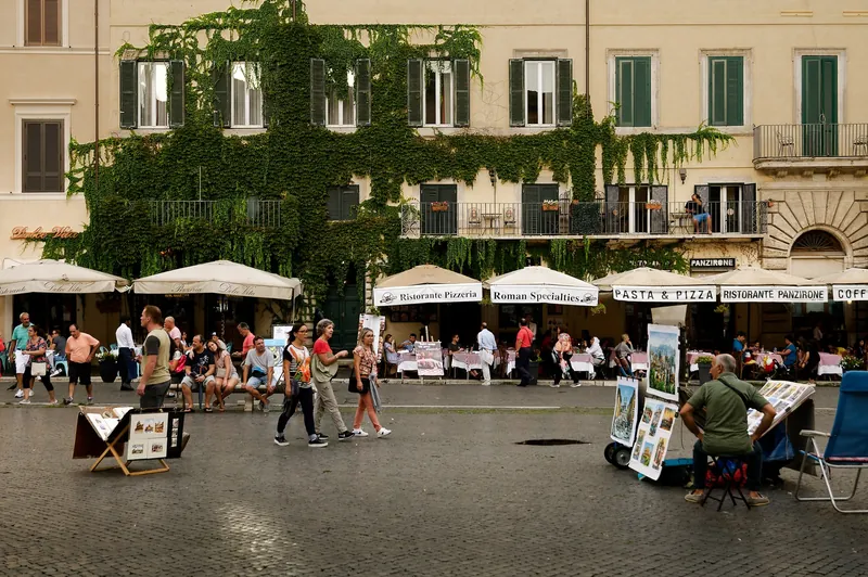 Wohnhäuser mit Restaurantterrassen und Straßenmalern an der Piazza Navona in Rom