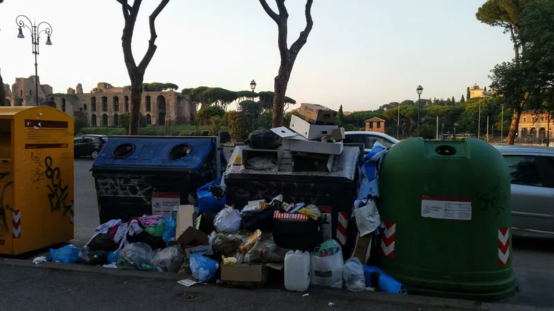 Überquellende Wertstoff- und Müllcontainer mit abgestellten Säcken und Kartons am Circus Maximus in Rom, im Hintergrund der Palatin