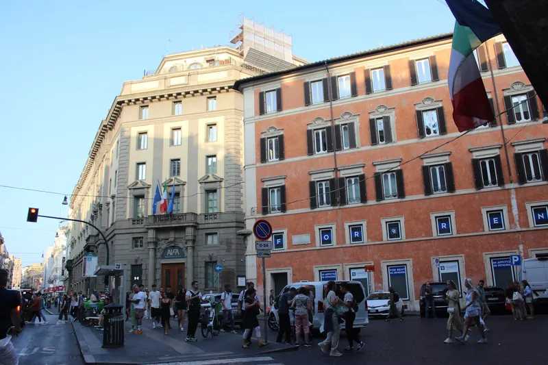 Street in central Rome with pedestrians, scooters and a palazzo with flats for rent (in affitto)