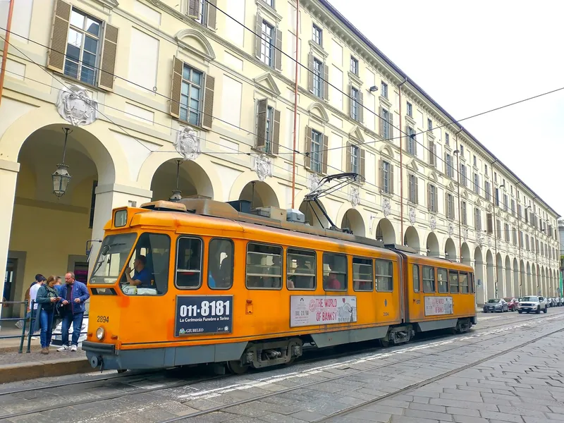 Historic orange series 2800 tram in front of an arcaded building in Turin