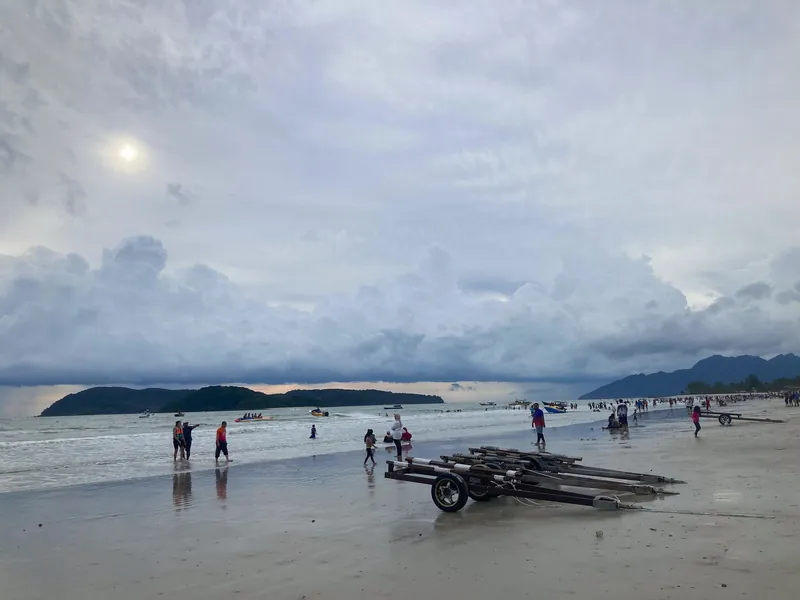 Badegäste und Bootsanhänger am Strand Pantai Cenang auf Langkawi bei Ebbe