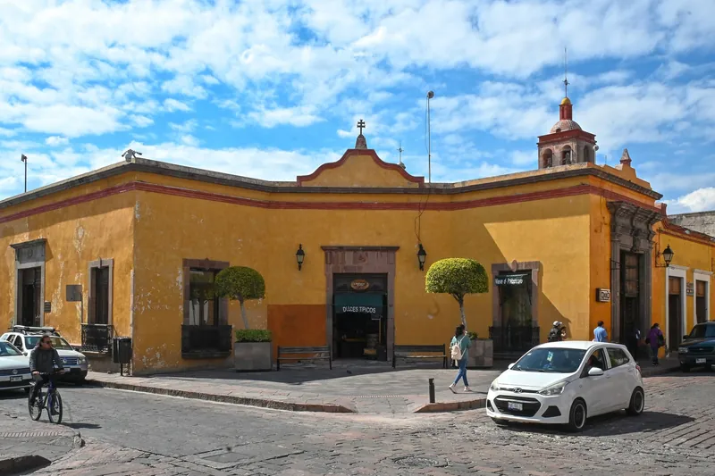 Ochre corner building with a sweet shop and a church tower in Querétaro's historic centre