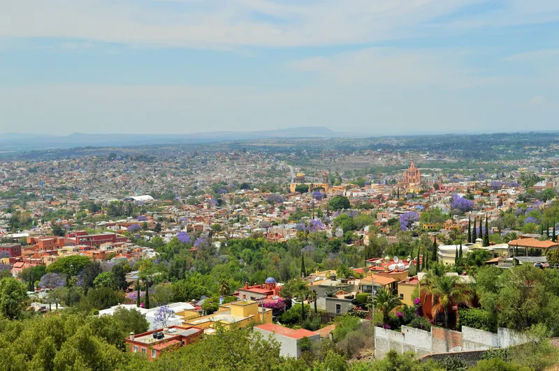 Blick von einem Aussichtspunkt im Südwesten über San Miguel de Allende mit blühenden Jacaranda-Bäumen