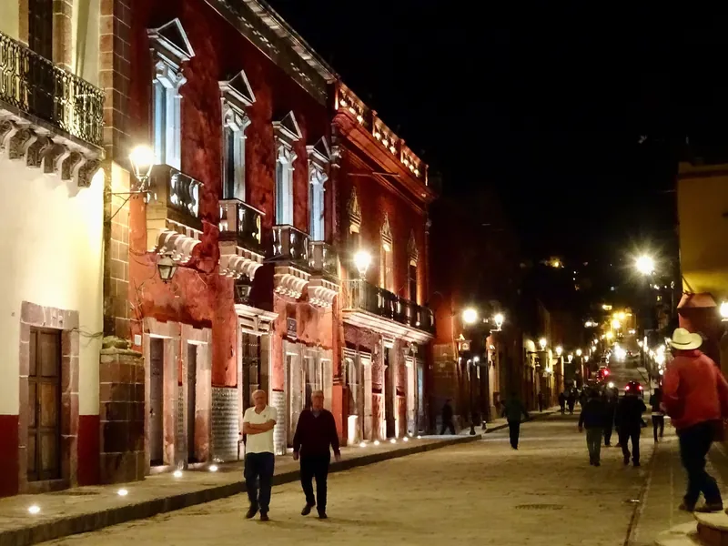Beleuchtete Altstadtstraße von San Miguel de Allende mit Passanten am Abend