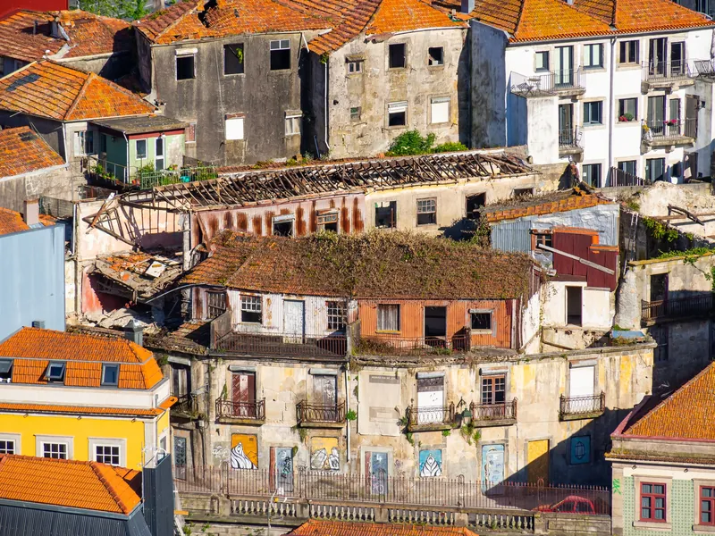 Verfallene Altbauten mit eingestürzten Dächern neben bewohnten Häusern im Viertel Morro da Sé in Porto