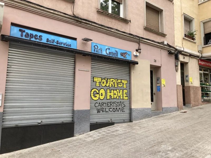 Graffiti „Tourist go home“ am Rollladen einer Tapasbar nahe dem Park Güell in Barcelona
