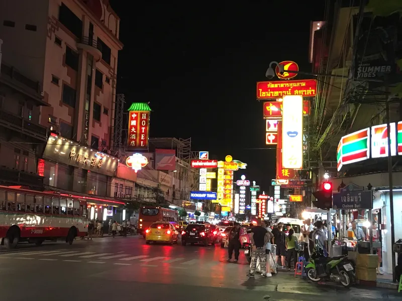 Yaowarat Road in Bangkoks Chinatown am Abend mit Leuchtreklamen, Verkehr und Straßenständen
