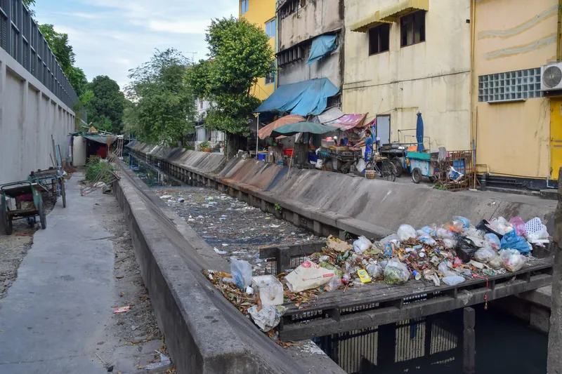 Müll in einem betonierten Kanal (Khlong) und auf einem Kanalgitter in Bangkok