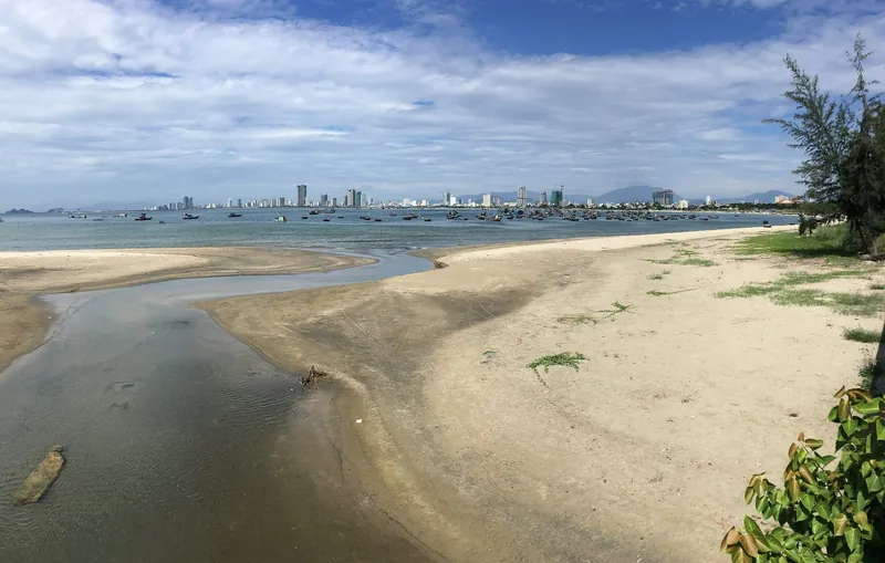 Flussmündung am Ende des Stadtstrands My Khe mit Fischerbooten und der Skyline von Da Nang