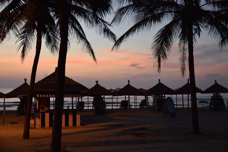 Strohschirme und Palmen am Strand von Da Nang bei Sonnenaufgang