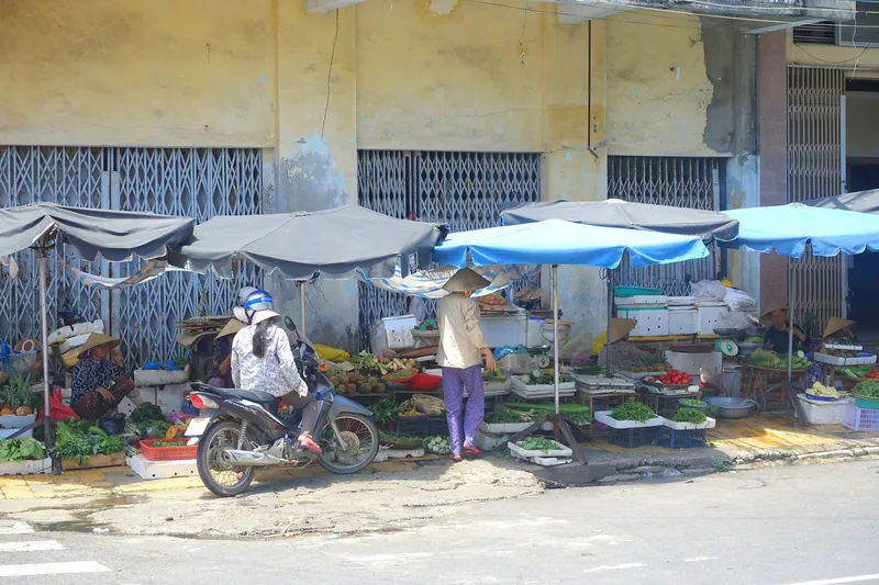 Straßenmarkt mit Gemüseständen und Sonnenschirmen vor einem Wohnblock in Da Nang