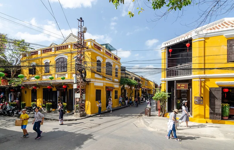 Gelb getünchte Kaufmannshäuser mit Lampions an einer Straßenecke der Altstadt von Hoi An